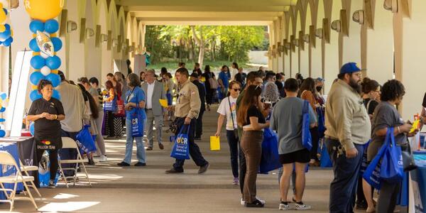 2022 Community Partner Fair attendees mingling with vendors below the Rivera Library arches