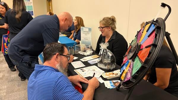 Community Partner Fair attendees filling out a form at a vendor table.