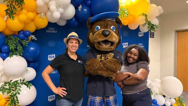 Two UCR staff members posing with Scotty Bear in front of the balloon arch photo booth.