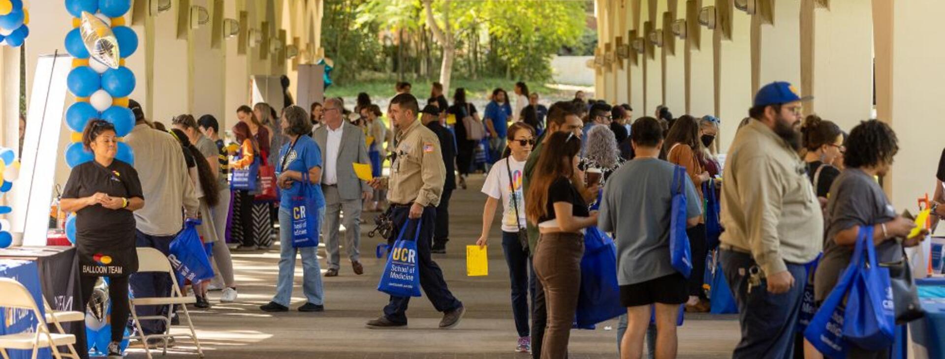 2022 Community Partner Fair attendees mingling with vendors below the Rivera Library arches