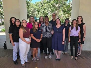 2025-2026 Staff Assembly Board, a group of thirteen people smiling under a shaded structure with trees in the background.